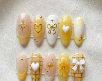 Paznokcie w żółte serduszka, urocze paznokcie w kształcie gwiazdek z kokardką, delikatne kwiatowe paznokcie, pastelowe letnie paznokcie, ręcznie robione paznokcie w kształcie migdałów