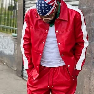 May include: Red leather jacket and matching pants with white stripes on the sleeves. The jacket has silver snap closures. The person is wearing a white undershirt and a bandana with the American flag design. The text "Leather FILE" is visible.