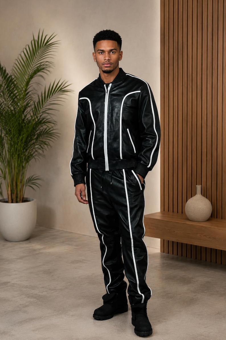 Peut inclure: Ensemble de surv&ecirc;tement en cuir noir avec passepoil blanc. La veste est zipp&eacute;e et le pantalon a une taille &agrave; cordon. La tenue est port&eacute;e avec des bottes noires. Le mod&egrave;le se tient dans une pi&egrave;ce moderne aux tons neutres.