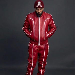 May include: A red leather tracksuit with white trim, featuring a zip-up jacket and matching pants. The outfit is paired with a maroon beanie with a skull and crossbones design. White sneakers complete the look. The text "LEATHER FILE" is visible.
