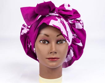 May include: A magenta head wrap with a white floral pattern and a large bow. The head wrap is on a mannequin head with a neutral skin tone. The background is white.