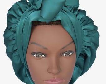 May include: Teal satin bonnet with a ruffled edge and a bow on top. The bonnet is designed to protect hair while sleeping. The satin material has a slight sheen. The bonnet is shown on a mannequin head.