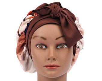 May include: A brown satin bonnet with a large bow on top, worn by a mannequin head. The bonnet has a patterned design in shades of red, white, and brown. The mannequin has brown eyes and a neutral expression.