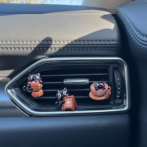 May include: Three black cat car air fresheners. One cat sits on a coffee cup, another on a coffee maker, and the third next to a sign that says "Coffee". The air fresheners are brown and black.