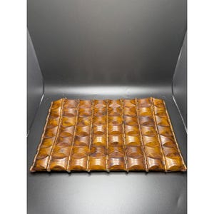 May include: A rectangular, wooden tray with a repeating pattern of rounded, rectangular indentations. The tray is a warm, medium brown color with variations in tone, suggesting a natural wood grain. The edges are slightly raised.