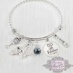 May include: Silver charm bracelet with a wine glass, letter A, black pearl, and a round charm that says "50 and Fabulous". The bracelet also has a small charm that says "Love".