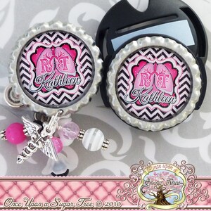 May include: Two pink and black patterned badge reels with a silver metal cap and a black retractable badge holder. The badge reels feature a pink lung with the letters "RT" and the name "Kathleen" in a black script font. The badge reels are attached to a silver chain with pink and white beads and a silver angel wing charm.