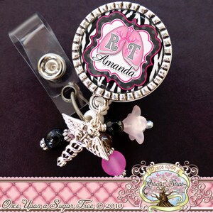 May include: A silver badge holder with a black and white zebra print design featuring pink lungs and the letters RT. The name Amanda is written below the lungs. The badge holder has a clear plastic clip and a silver chain with pink and black beads.
