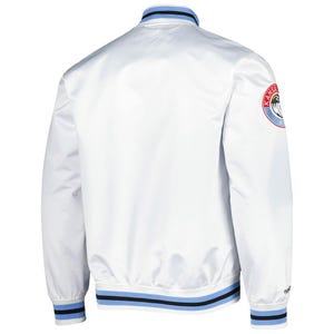 Puede incluir: Una chaqueta bomber de sat&eacute;n blanco con cuello alto y ribetes a rayas en azul claro y negro. Los pu&ntilde;os y el dobladillo tambi&eacute;n muestran rayas a juego en azul claro y negro. Un parche circular con texto en rojo, blanco y azul est&aacute; en la manga izquierda.