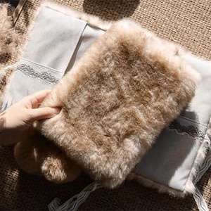 May include: A rectangular pouch featuring a thick, light brown faux fur exterior on one side and a smooth, light grey fabric on the other. The grey section is accented with a delicate white lace trim detail along the centre of the panel.