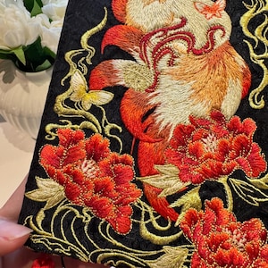 May include: Black fabric with detailed embroidery of a fox, butterflies, and flowers in red, orange, and gold. The design is ornate, with a focus on floral and animal motifs, showcasing a rich colour palette.