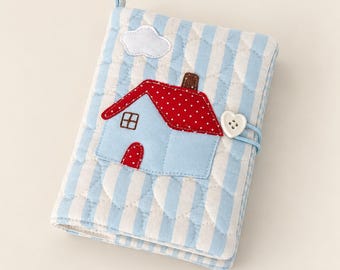 May include: A quilted fabric notebook cover featuring light blue and white vertical stripes with a heart-shaped stitching pattern. An appliqué of a light blue house with a red polka-dot roof, a white cloud, and a white heart-shaped button closure.