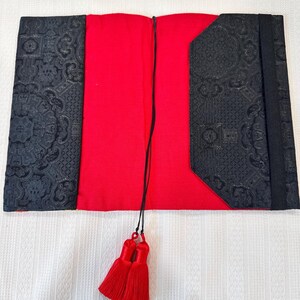 May include: Open book cover with a red interior and black patterned exterior. The black covers have an ornate design. Red tassels hang from the spine. The book cover is open and lying flat.