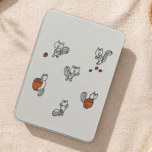 May include: A white tablet case featuring cartoon squirrels with acorns. The squirrels are in various poses, some holding acorns, others with their tails up. The design is in black and orange on a white background.
