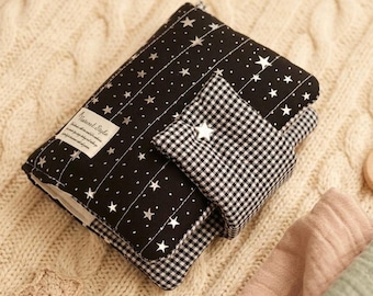 May include: A black fabric pouch featuring a white star pattern and vertical stitching, with a black and white gingham check flap closure. A small rectangular label with the text Natural Style is attached to the front, and a single star button.
