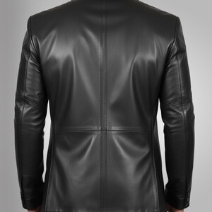 K&ouml;nnte beinhalten: Ein schwarzer Lederblazer mit klassischem Design. Die Jacke hat ein fallendes Revers, lange &Auml;rmel und einen Zwei-Knopf-Verschluss. Der R&uuml;cken des Blazers hat einen Mittelschlitz und eine taillierte Passform. Das Leder wirkt glatt und hat einen leichten Glanz.