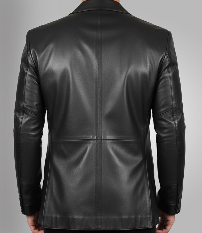 K&ouml;nnte beinhalten: Ein schwarzer Lederblazer mit klassischem Design. Die Jacke hat ein fallendes Revers, lange &Auml;rmel und einen Zwei-Knopf-Verschluss. Der R&uuml;cken des Blazers hat einen Mittelschlitz und eine taillierte Passform. Das Leder wirkt glatt und hat einen leichten Glanz.