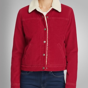 May include: A red corduroy jacket with a cream-colored, sherpa-lined collar. The jacket has a button-up front, two chest pockets, and long sleeves. The model is wearing blue jeans. The jacket is a classic style.