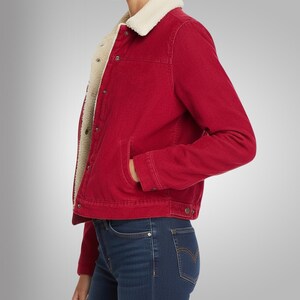 May include: A red corduroy jacket with a cream-colored, fuzzy lining and collar. The jacket has a button-up front, two front pockets, and long sleeves. The model is wearing blue jeans.