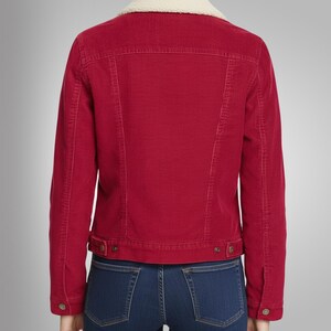 May include: A red corduroy jacket with a cream-colored, fuzzy collar. The jacket has a button closure and two front pockets. The model is wearing blue jeans. The jacket is a classic style.