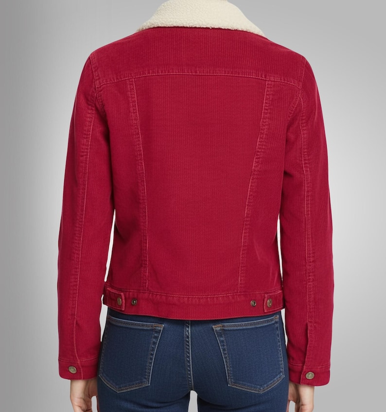 May include: A red corduroy jacket with a cream-colored, fuzzy collar. The jacket has a button closure and two front pockets. The model is wearing blue jeans. The jacket is a classic style.