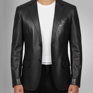 K&ouml;nnte beinhalten: Ein schwarzer Lederblazer mit Zwei-Knopf-Verschluss, fallendem Revers und Brusttasche. Der Blazer hat lange &Auml;rmel und zwei Vordertaschen. Darunter wird ein wei&szlig;es T-Shirt getragen.