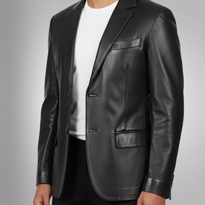 K&ouml;nnte beinhalten: Ein schwarzer Lederblazer mit Zwei-Knopf-Verschluss, Revers und Brusttasche. Der Blazer wird &uuml;ber einem wei&szlig;en T-Shirt getragen. Die Jacke hat eine klassische, taillierte Passform.