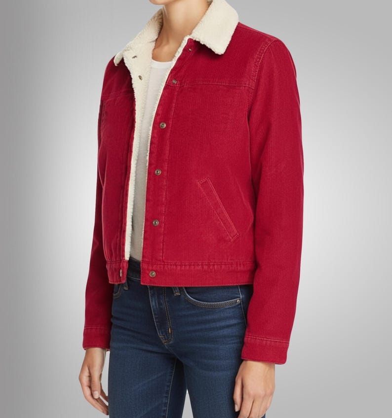May include: A red corduroy jacket with a cream-colored, fuzzy collar and lining. The jacket has a button-up front, two front pockets, and long sleeves. The model is wearing blue jeans and a white t-shirt underneath.