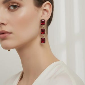 May include: Long, drop earrings with three rectangular, deep red gemstones set in a gold-coloured metal. These earrings are a statement piece, adding glamour and sophistication to any outfit.