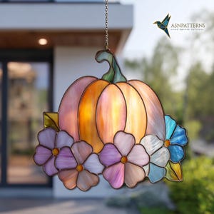 K&ouml;nnte beinhalten: H&auml;ngende Glas-K&uuml;rbis-Dekoration. Der K&uuml;rbis besteht aus orangefarbenem und rosa Glas mit einem gr&uuml;nen Stiel. Die Basis ist mit Blumen in Lila-, Rosa- und Blaut&ouml;nen verziert. Ein dekoratives St&uuml;ck f&uuml;r den Herbst.