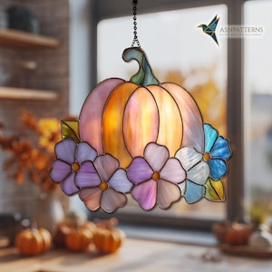 K&ouml;nnte beinhalten: Ein Glasfenster-Sonnenf&auml;nger in K&uuml;rbisform, an einer Kette aufgeh&auml;ngt. Der K&uuml;rbis besteht aus orangefarbenem und rosa Glas mit einem gr&uuml;nen Stiel und Bl&auml;ttern. Er ist mit lila, rosa und blauen Blumen verziert. Der Text "ASNPatterns" ist sichtbar.