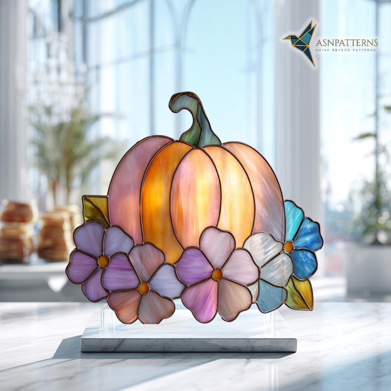 K&ouml;nnte beinhalten: Buntglas-K&uuml;rbis mit gr&uuml;nem Stiel und bunten Blumen. Der K&uuml;rbis ist eine Mischung aus Orange, Rosa und Gelb. Die Blumen sind in Lila-, Rosa- und Blaut&ouml;nen gehalten. Pr&auml;sentiert auf einem wei&szlig;en Marmorsockel.
