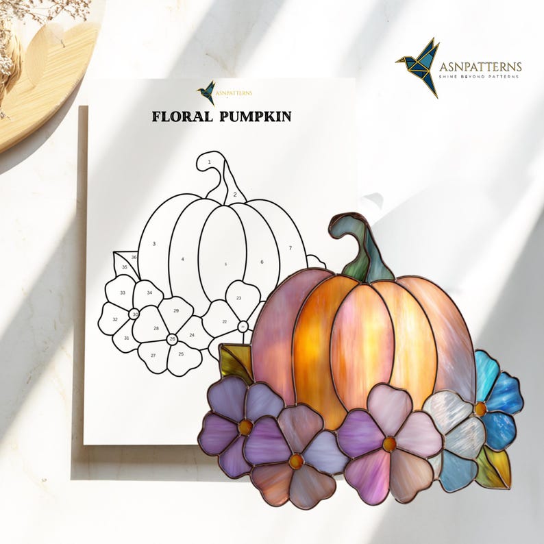 K&ouml;nnte beinhalten: Ein Buntglas-Blumenk&uuml;rbis in Orange-, Rosa- und Lilat&ouml;nen, umgeben von lila und blauen Blumen. Im Hintergrund ein Papier mit den Worten "FLORAL PUMPKIN" und einer K&uuml;rbiskontur.
