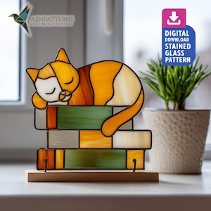 May include: Stained glass cat figurine in orange, white, and brown, sleeping on a stack of green, yellow, and gray blocks. The figurine sits on a wooden base. The image includes the text "DIGITAL DOWNLOAD STAINED GLASS PATTERN".