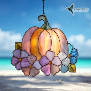 K&ouml;nnte beinhalten: Buntglas-K&uuml;rbis-Dekoration mit gr&uuml;nem Stiel und Kette zum Aufh&auml;ngen. Der K&uuml;rbis ist eine Mischung aus Orange und Rosa, mit bunten Blumen in Lila-, Wei&szlig;- und Blaut&ouml;nen.