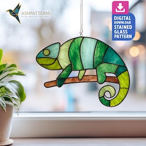 May include: A stained glass chameleon in shades of green, blue, and yellow, perched on a brown branch. The artwork is hanging in front of a window. The image includes the text "DIGITAL DOWNLOAD STAINED GLASS PATTERN".