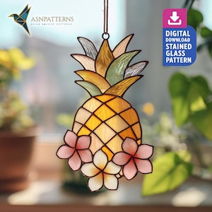 Op de afbeelding: Een gebrandschilderde glazen ananas zonnevanger met een gele en oranje body, groene en bruine kroon en roze en witte bloemen. De zonnevanger hangt aan een bruin touwtje. De afbeelding bevat ook de tekst "DIGITAL DOWNLOAD STAINED GLASS PATTERN".