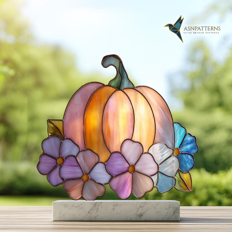 K&ouml;nnte beinhalten: Ein Buntglas-K&uuml;rbis mit gr&uuml;nem Stiel und farbigen Paneelen in Orange, Rosa und Gelb. Der K&uuml;rbis ist mit lila, blauen und wei&szlig;en Blumen verziert. Das Kunstwerk wird auf einem wei&szlig;en Marmorsockel ausgestellt.
