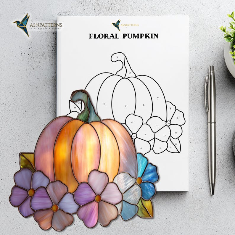 K&ouml;nnte beinhalten: Ein Buntglas-K&uuml;rbis mit lila, blauen und rosa Blumen. Der K&uuml;rbis ist orange und rosa mit einem gr&uuml;nen Stiel. Eine Malbuchseite mit einer K&uuml;rbiskontur und den Worten "FLORAL PUMPKIN" befindet sich im Hintergrund.