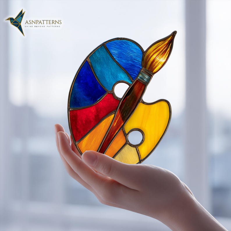 May include: A colorful stained glass art palette and paintbrush. The palette features sections of blue, red, orange, and yellow. The paintbrush has a brown handle and a golden-yellow bristle. The logo "ASN PATTERNS" is in the upper left corner.
