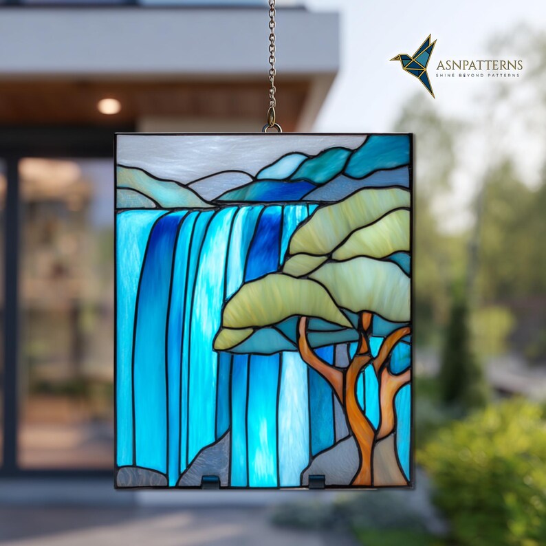 May include: Stained glass panel showing a waterfall scene. The artwork features a vibrant blue waterfall cascading down, with a tree in the foreground. The panel is framed in black and hangs from a chain. The top of the panel has the text "ASNPatterns Shine Beyond Patterns".