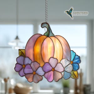 K&ouml;nnte beinhalten: H&auml;ngende Glas-K&uuml;rbis-Dekoration mit Kette. Der K&uuml;rbis hat orange- und rosafarbene Farbt&ouml;ne mit einem gr&uuml;nen Stiel. Verziert mit bunten Blumen in Lila, Blau und Wei&szlig;. Ein dekoratives Element f&uuml;r Herbstdekoration.