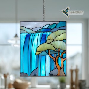 May include: Stained glass panel showing a waterfall scene with blue and turquoise water. A tree with yellow-green leaves and an orange trunk is on the right. The panel is framed in black and hangs from a silver chain.