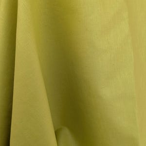 Könnte beinhalten: Nahaufnahme eines gefalteten, einfarbigen Stoffes in einem Farbton von Chartreusegrün. Der Stoff hat eine subtile Textur und scheint Leinen oder ein ähnliches Material zu sein. Die Falten erzeugen Schatten und Glanzlichter und verleihen dem Bild Tiefe.