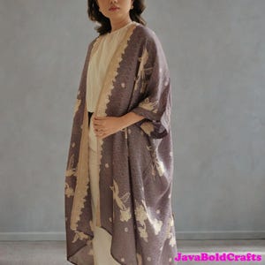May include: A long, open-front kimono in a muted purple hue, featuring a repeating pattern and floral accents in a lighter shade. The edges are trimmed with a beige, decorative border. The text "JavaBoldCrafts" is visible in the lower right corner.