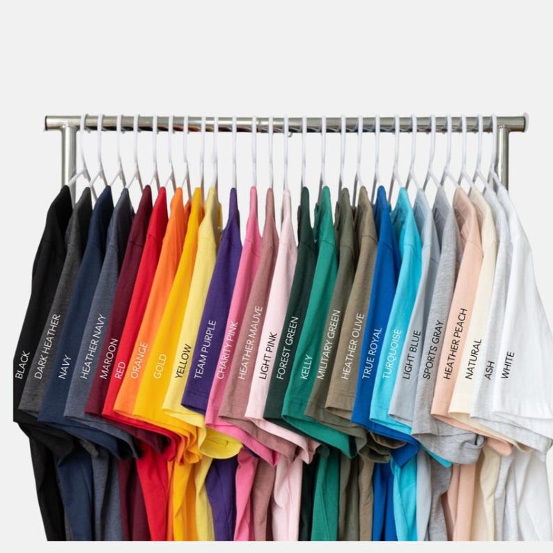 May include: A rack of various colored t-shirts, including black, navy, red, yellow, and white. Each shirt is neatly hung on a white hanger. The colors are labeled with their names.