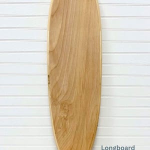 May include: A longboard made of natural wood. The board is light brown and has a smooth, rounded shape. The word "Longboard" is printed in blue text on the bottom right corner of the board.