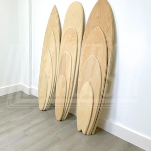May include: Four wooden balance boards of varying sizes are stacked against a white wall. The boards are made of light wood and have a rounded shape. The boards are arranged in order of size, with the largest board at the bottom and the smallest board at the top. The boards are all leaning against the wall, and the bottom board is slightly tilted forward. The boards are all made of the same type of wood, and they have a smooth, polished finish. The boards are all in good condition, and they appear to be new. The boards are all in focus, and the background is blurred.