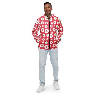 May include: A red zip-up jacket with a repeating pattern of white circles, each containing a red and green design. The jacket is worn with light blue jeans and white sneakers. The person is smiling.