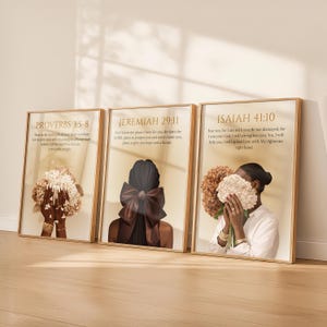 May include: Three framed art prints with gold frames. Each print features a woman and a floral bouquet. The prints display Bible verses: Proverbs 3:5-8, Jeremiah 29:11, and Isaiah 41:10. The background is a light beige color.